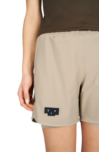 Women's running shorts in Warm Sand, featuring an inner lining and side vents. The 5-inch Flow Shorts offer a soft stretch and are made from ECONYL®. Podium Logo on the front and a reflective "Finish in a Good Place" slogan on the back. Includes one pocket in the inner lining and a hidden pocket at the back. Also available in a 3-inch length.