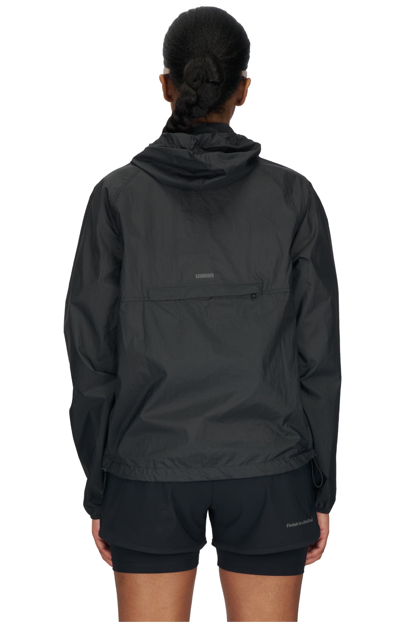 Women's ultra-lightweight running jacket (55g/m²) in Black. It features an adjustable hood, two side pockets, a back pocket, and side vents for enhanced ventilation. It is equipped with adjustable straps at the hem for a customizable fit. Made from 100% recycled nylon, it offers protection against wind and light rain. Additionally, it is packable, PFC-free, and features a reflective UNNA logo on the back, along with a UNNA patch on the zipper