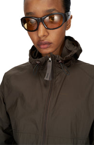 Women's ultra-lightweight running jacket (55g/m²) in Wren Brown. It features an adjustable hood, two side pockets, a back pocket, and side vents for enhanced ventilation. It is equipped with adjustable straps at the hem for a customizable fit. Made from 100% recycled nylon, it offers protection against wind and light rain. Additionally, it is packable, PFC-free, and features a reflective UNNA logo on the back, along with a UNNA patch on the zipper